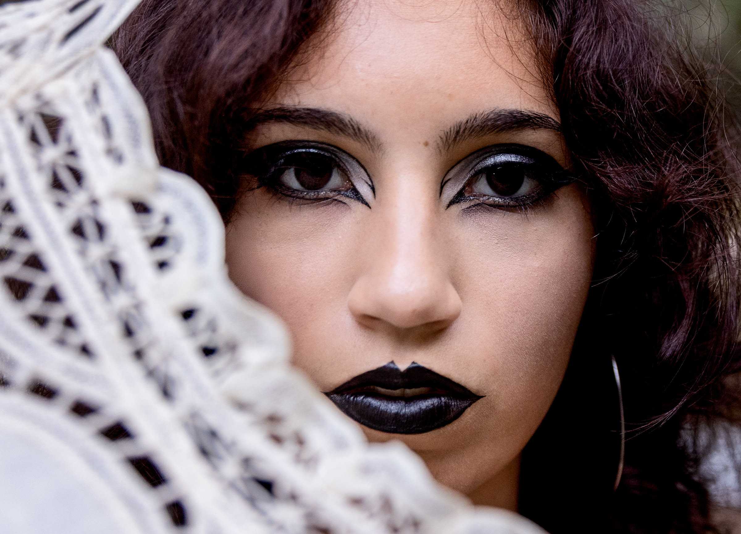 A Nature’s Child Photography senior portrait featuring a dramatic close-up of a high school senior with bold black lipstick and artistic eye makeup, creating an edgy gothic look during a cemetery session in Amelia Island Florida